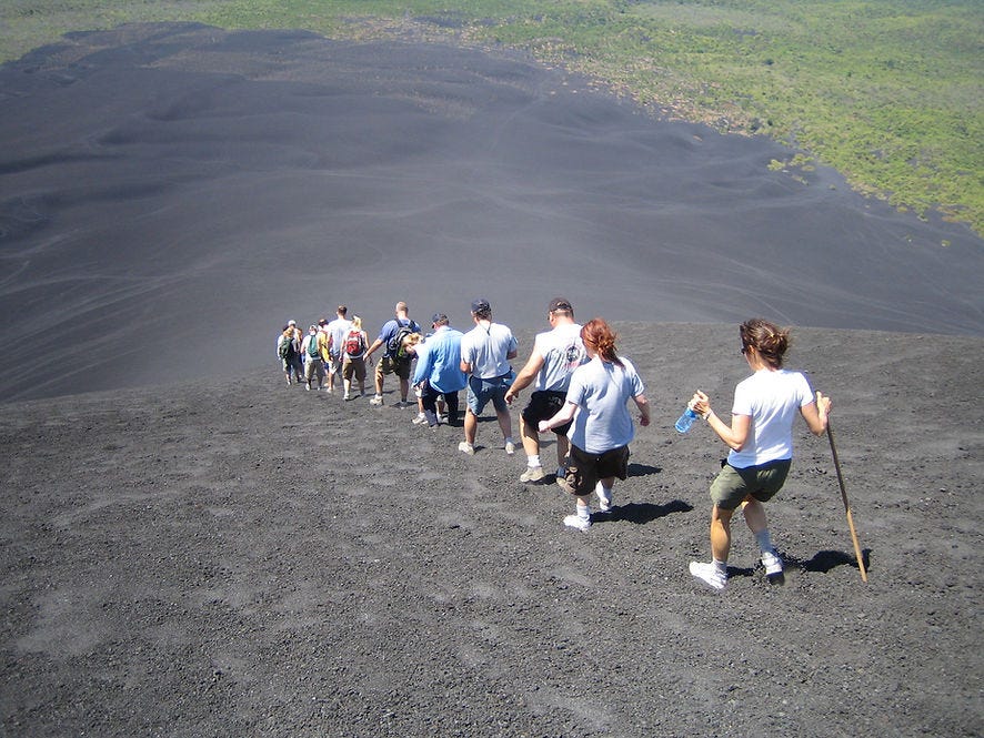 single file line of people hiking down side of volcano