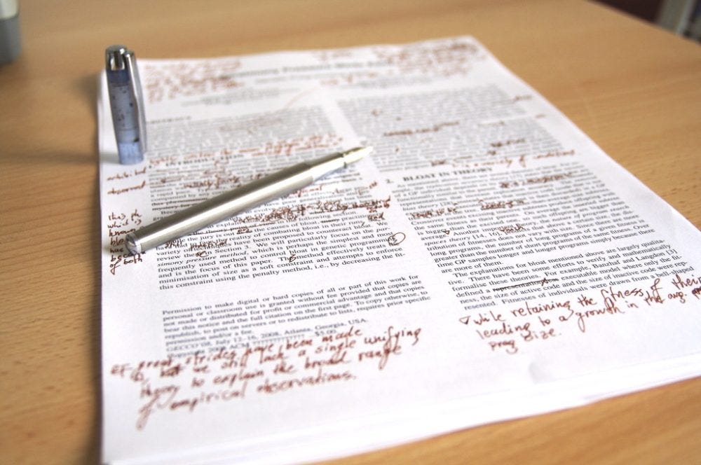A picture of a sheet of writing with a pen and edits scribbled in red ink A picture of a sheet of writing with a pen and edits scribbled in red ink