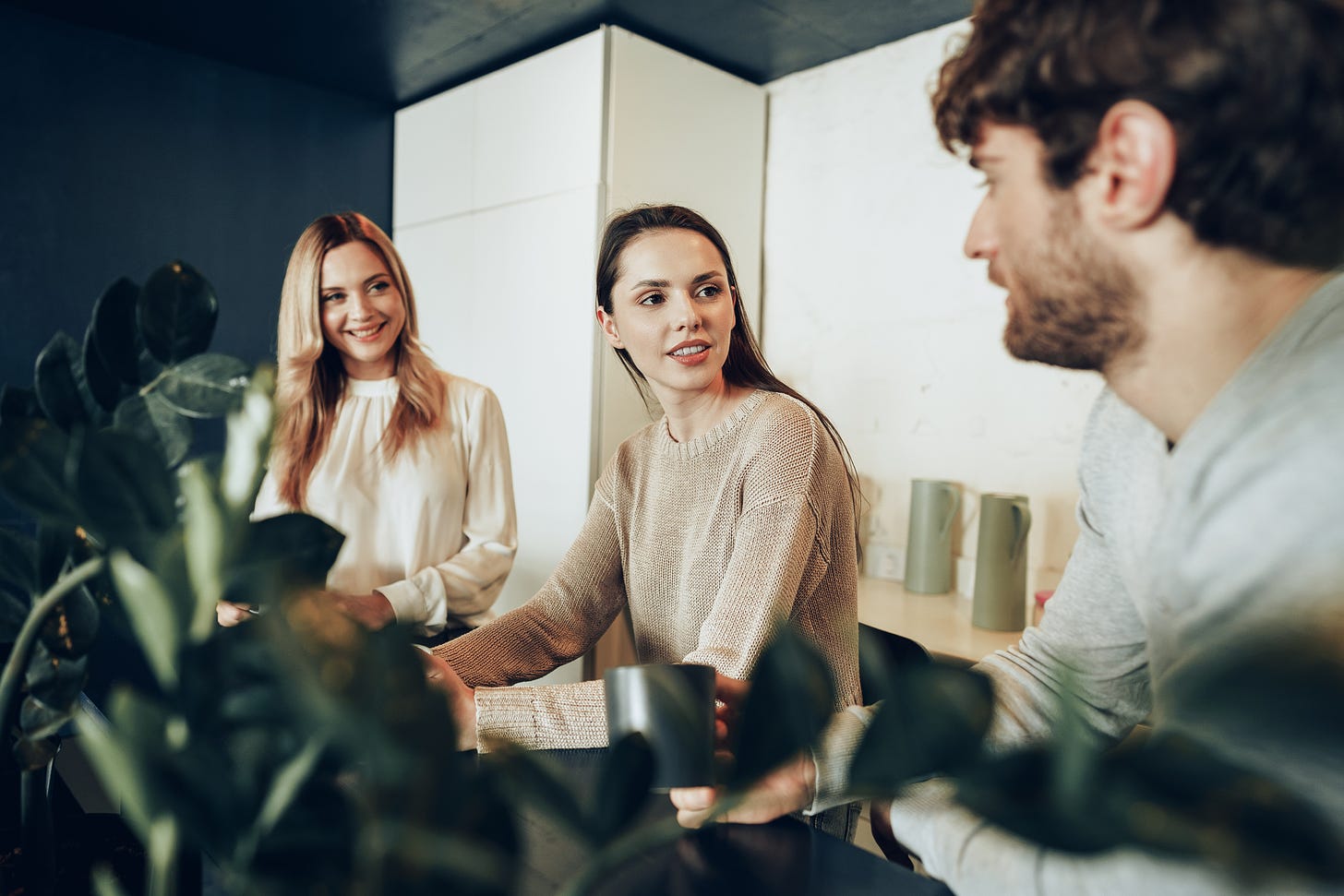 Photo of three people talking and drinking coffee in an office
