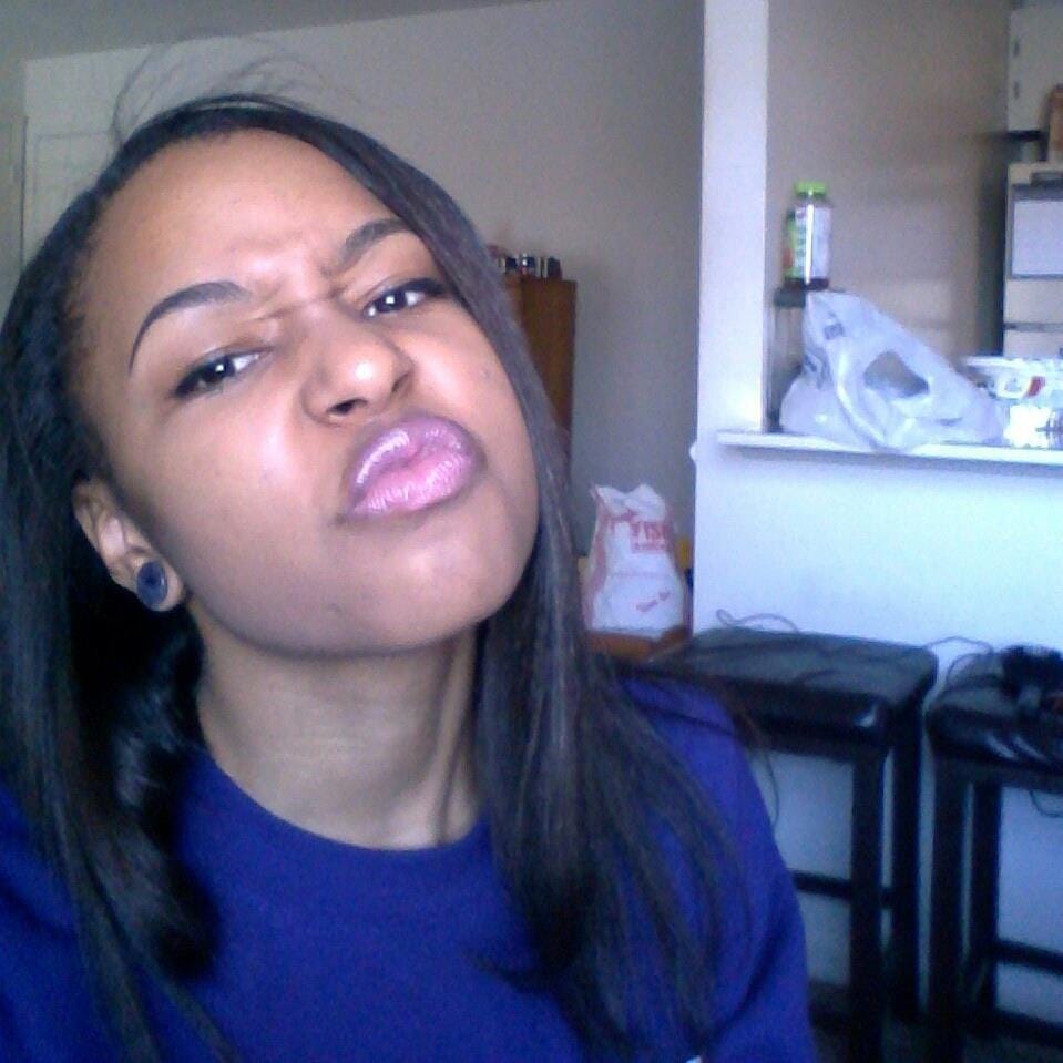 A black girl making a scrunched face at the camera with straightened hair and in a purple sweatshirt