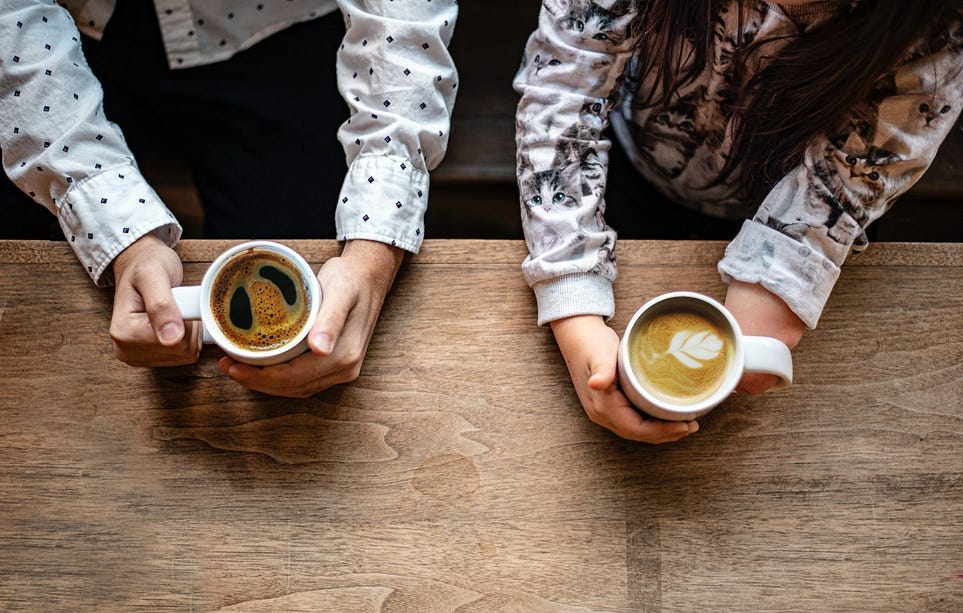 Image shows two people’s hands holding coffee mugs on a table. One person has had their hand amputated.