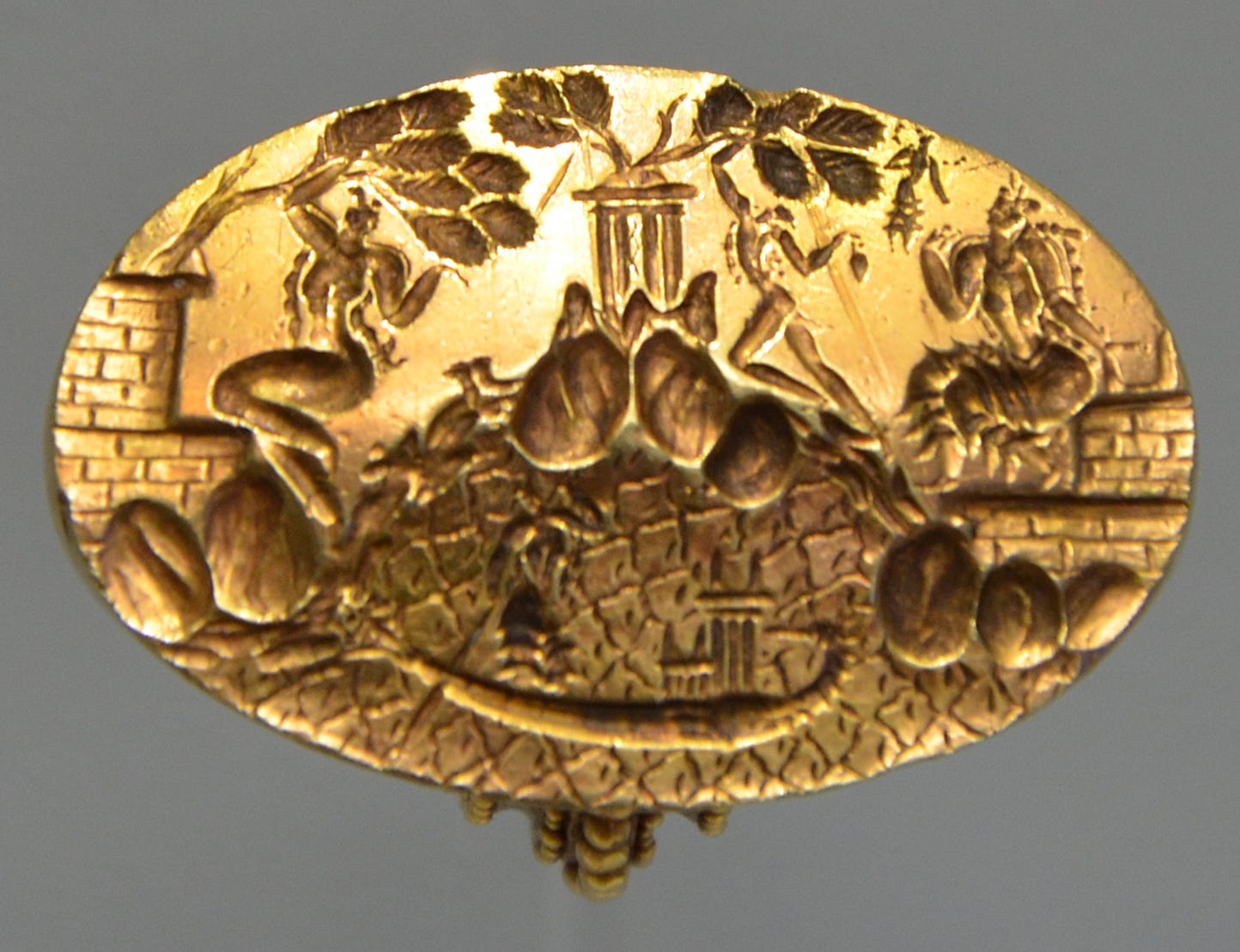 An oval gold ring with a scene featuring, in the center, a woman standing next to a small shrine in a reed boat on the water. Behind her, on the shore, a woman and a man perform tree-shaking rituals, bending tree branches down, while a seated priestess is approached by a tiny floating goddess.