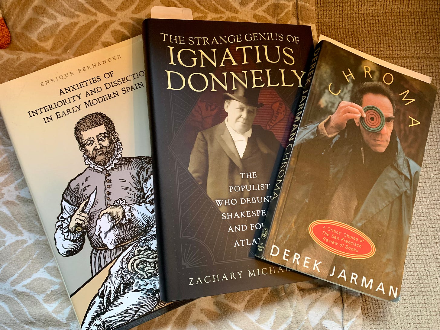 Three books spread out in a fan shape: Anxieties of Interiority and Dissection in Early Modern Spain by Enrique Fernandez, The Strange Genius of Ignatius Donnelly by Zachary Michael Jack, and Chroma by Derek Jarman