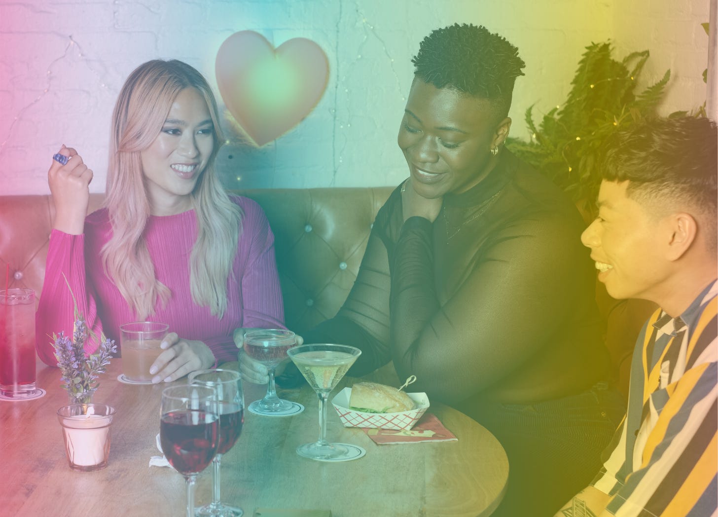 A rainbow-filtered imaged of three diverse people seated at a table in a cozy, warmly lit setting smiling and enjoying drinks, with one person holding a cocktail and another holding a coop glass.