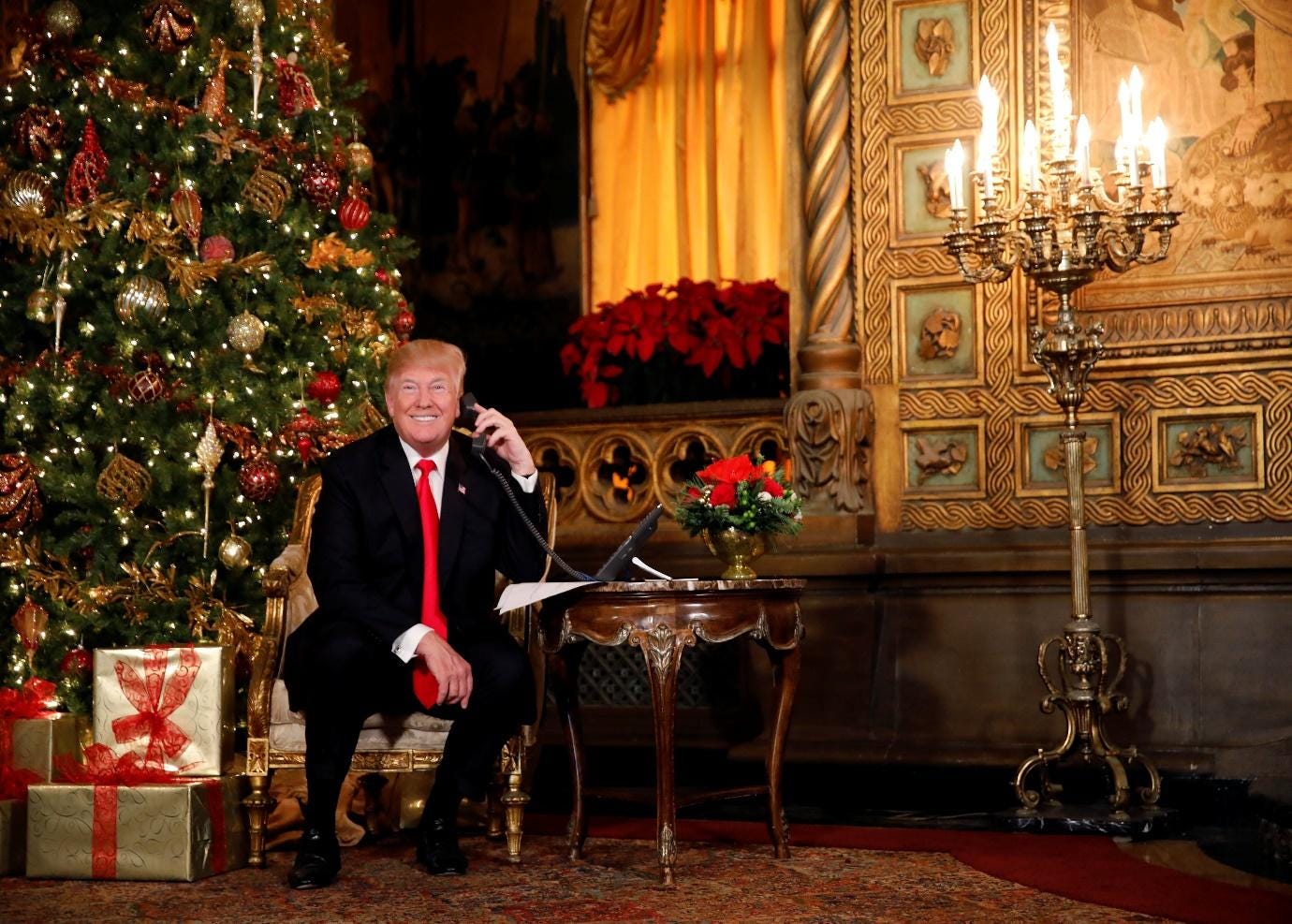 A person in a suit and tie sitting in a chair with a christmas tree

Description automatically generated