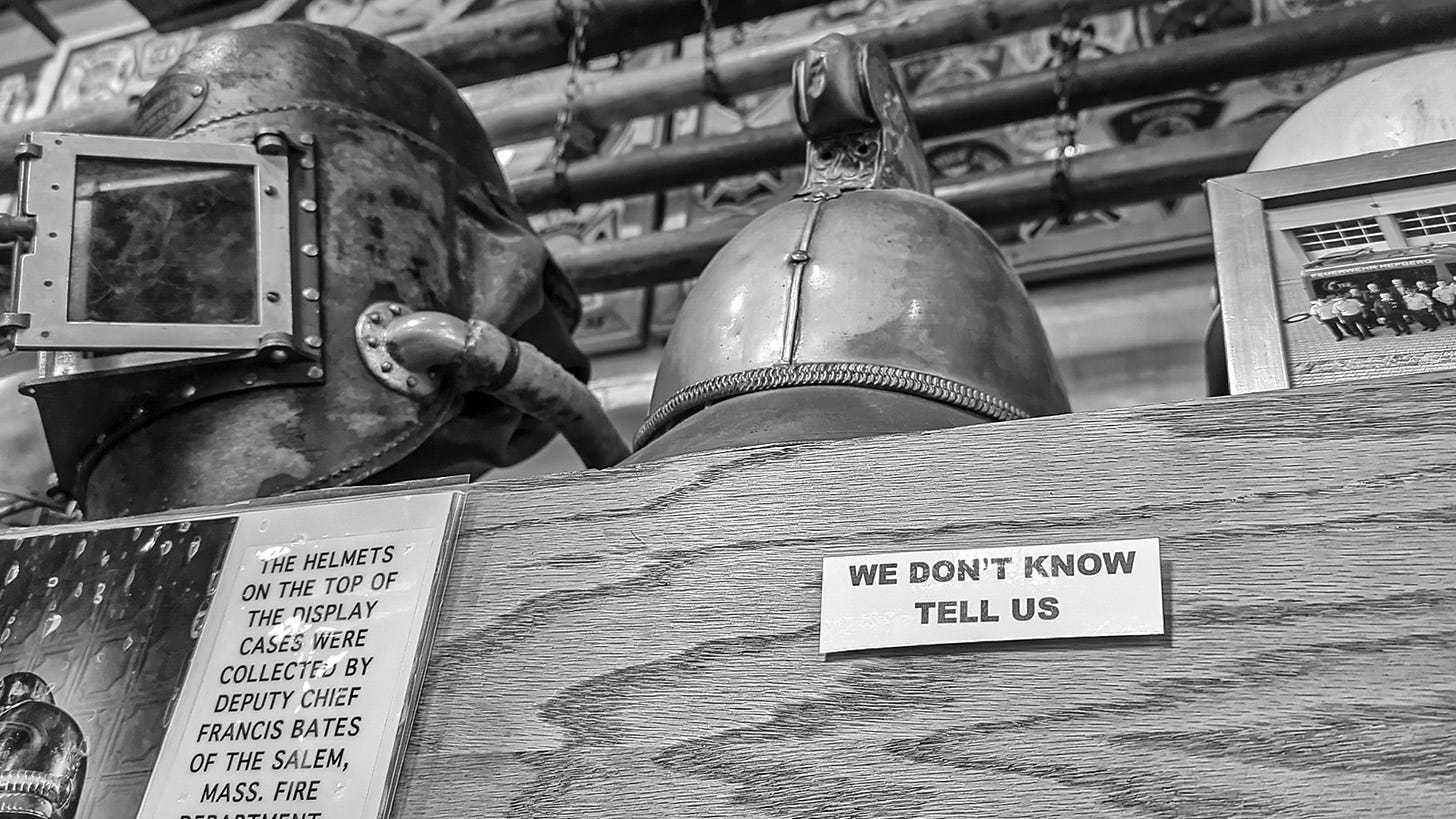 Helmets from another world sit on a shelf with a sign that reads "WE DON'T KNOW. TELL US"