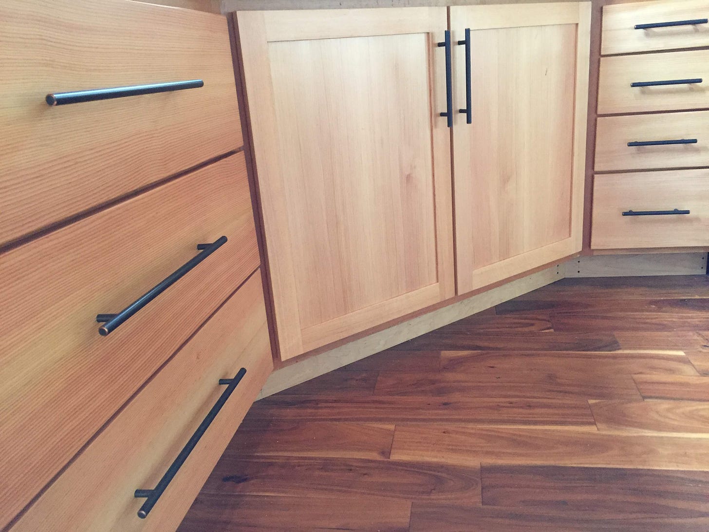 close up of a line of kitchen cabinets and drawers, with straight grained cedar wood and modern black iron hardware