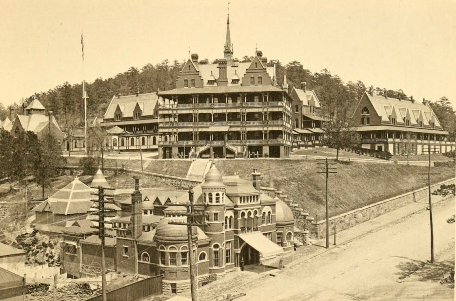 A sepia photograph of some opulent buildings with domes and turrets. The building in the background has balconies all round each floor.