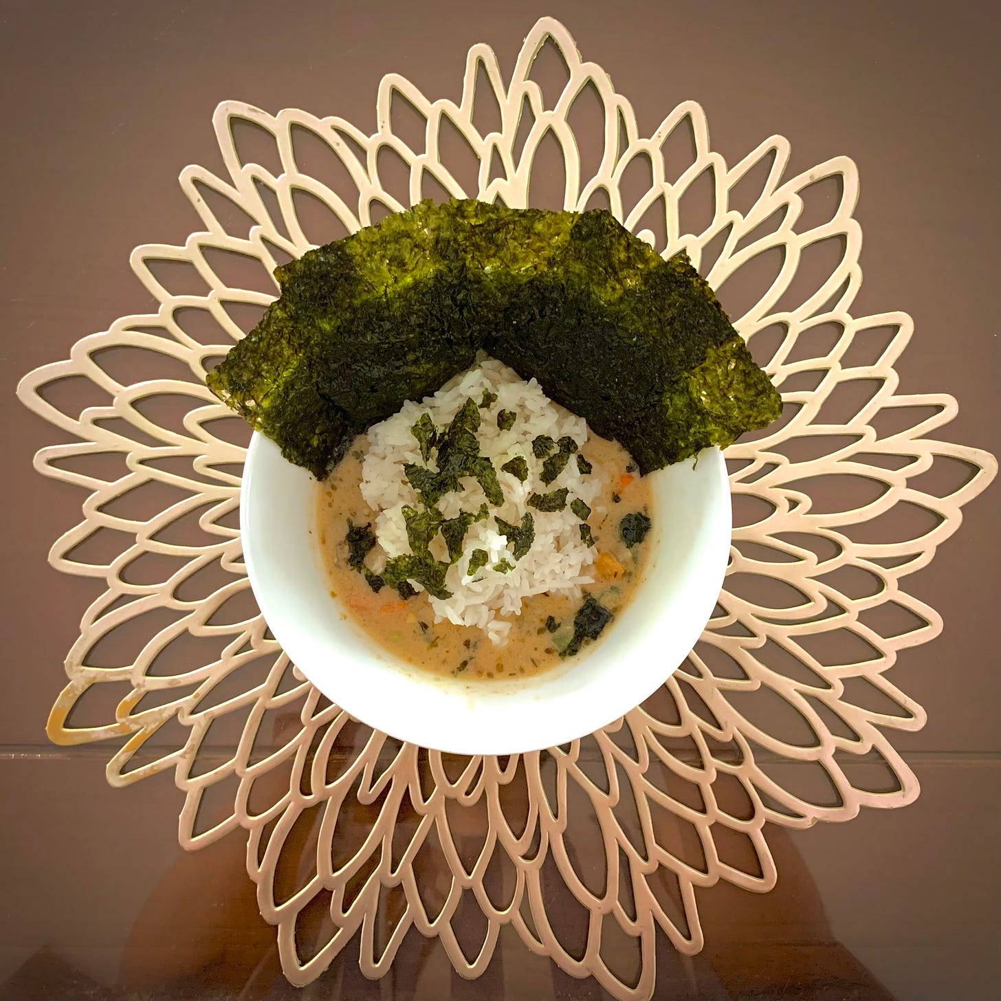 A picture of a bowl rice in soup and a few sheets of nori.