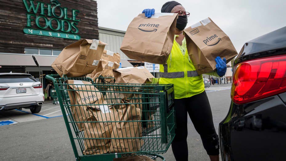 An independent contractor wearing a protective mask and gloves loads Amazon Prime grocery bags into a car outside a Whole Foods Market in Berkeley, California, Oct. 7, 2020.