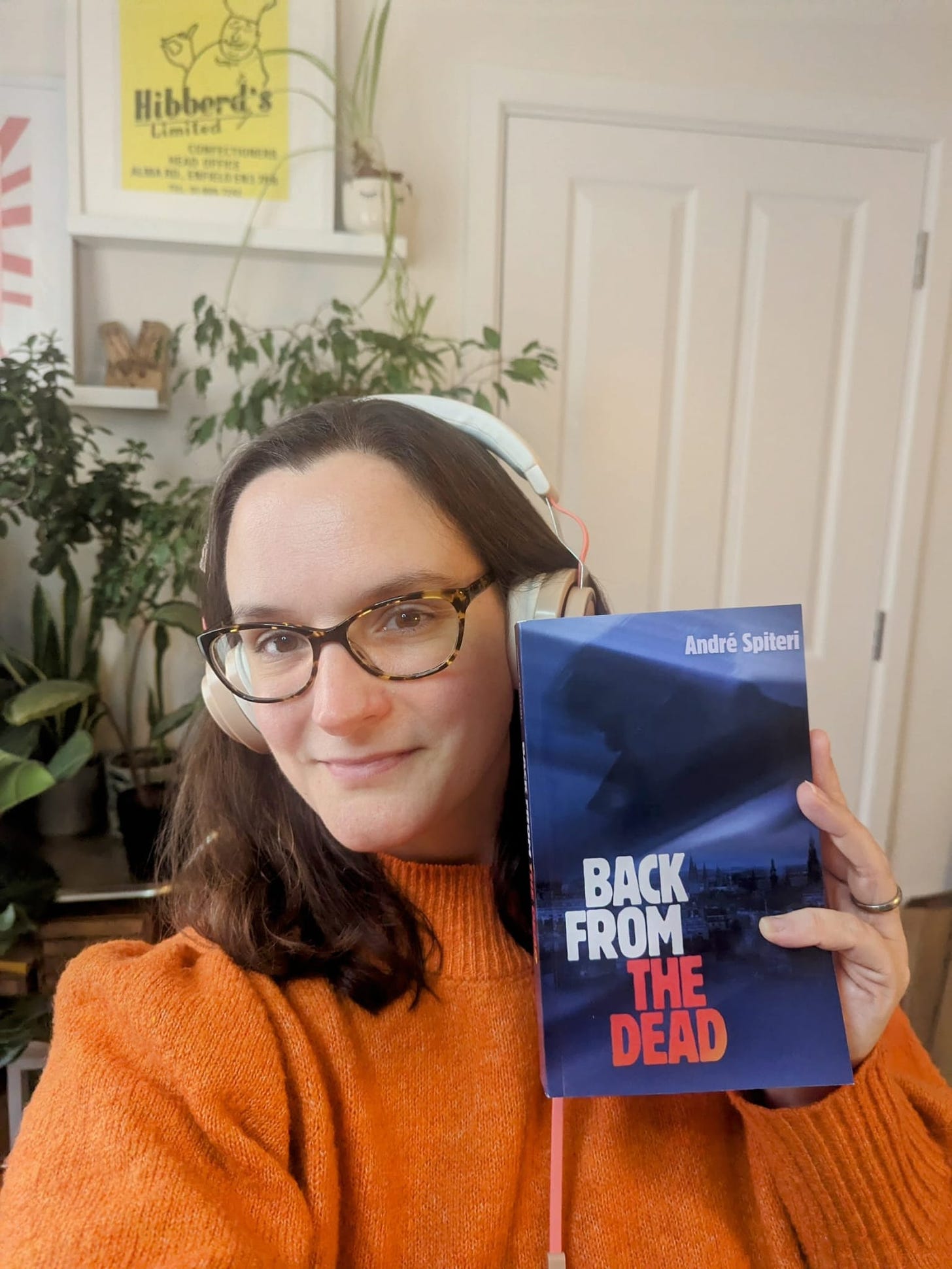 Mel Barfield in an orange jumper holding a blue book called Back from the Dead by Andre Spiteri