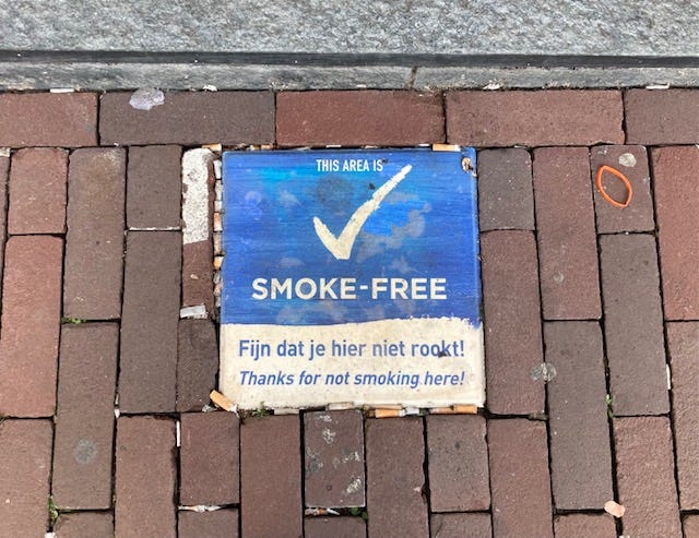 the image shows a Smoke-free sign on the road is littered with cigarettes. the ministry is enacting laws to limit smoking in the netherlands