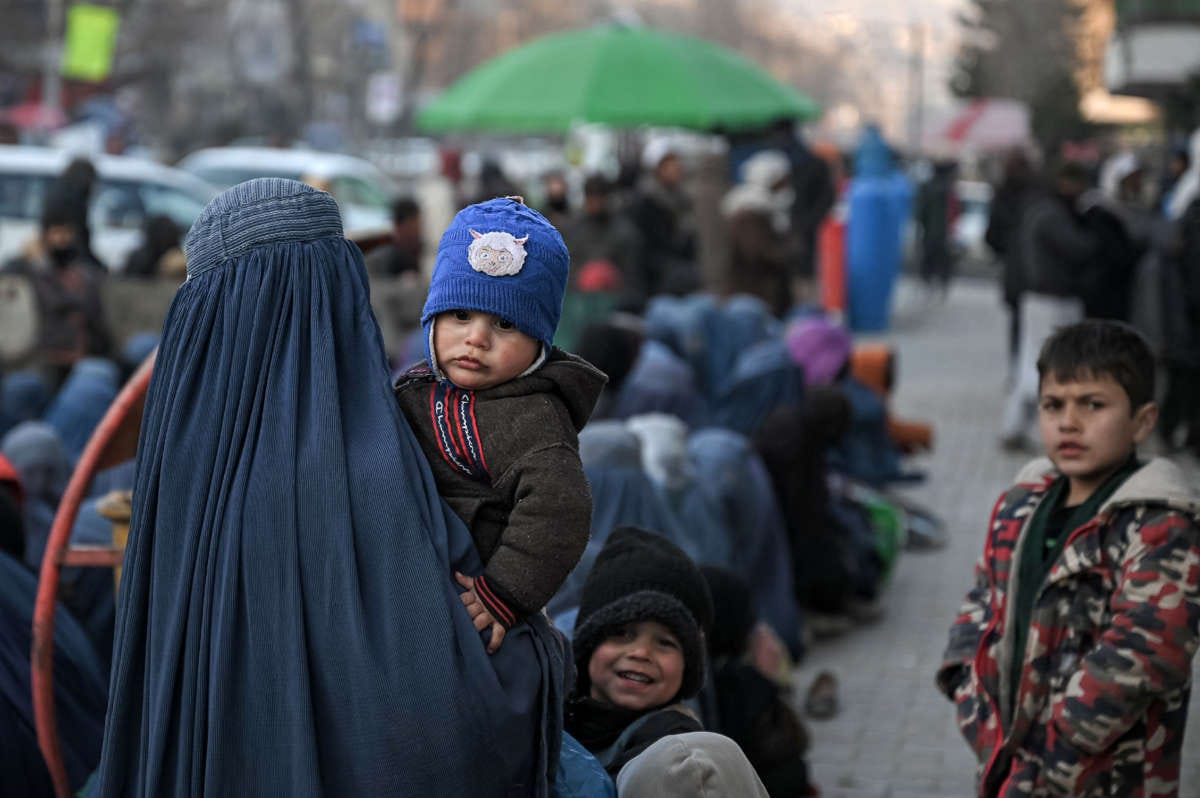 A woman wearing a burqa carries an infant as she waits with others for free bread in front of a bakery in Kabul, Afghanistan, on January 24, 2022. A woman wearing a burqa carries an infant as she waits with others for free bread in front of a bakery in Kabul, Afghanistan, on January 24, 2022.