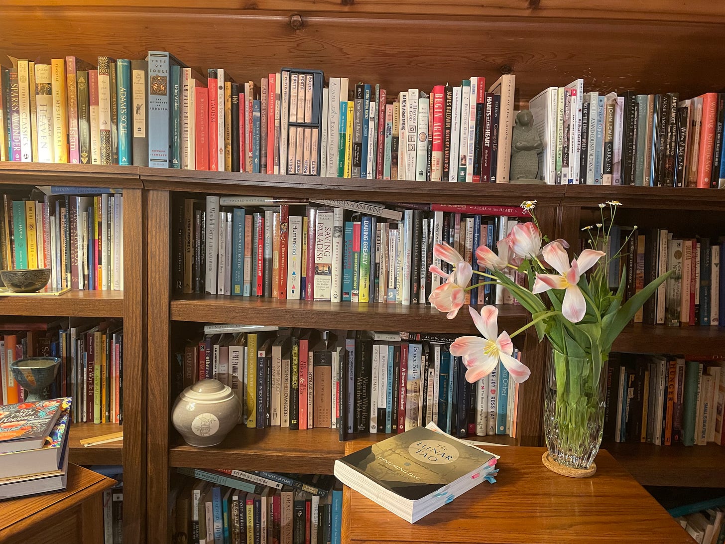 A wall of bookshelves with a table in front holding another book and a vase of flowers