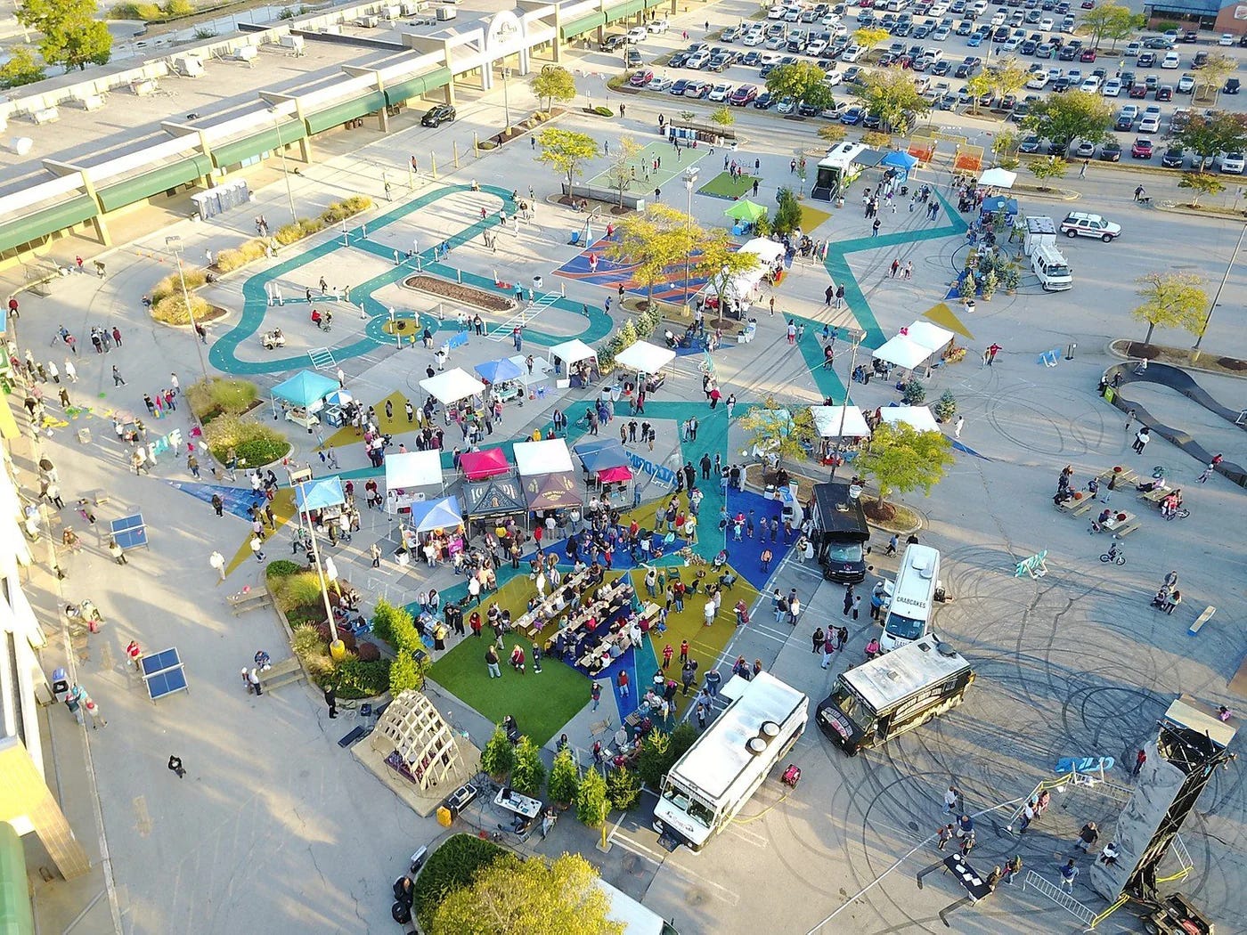 An overhead shot of a giant parking lot, into which Better Block have painted bike paths, kiosks and tents for play, temporary turf and picnic tables.