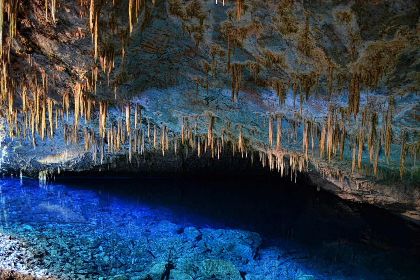 A cave full of stalactites hanging above a blue pool