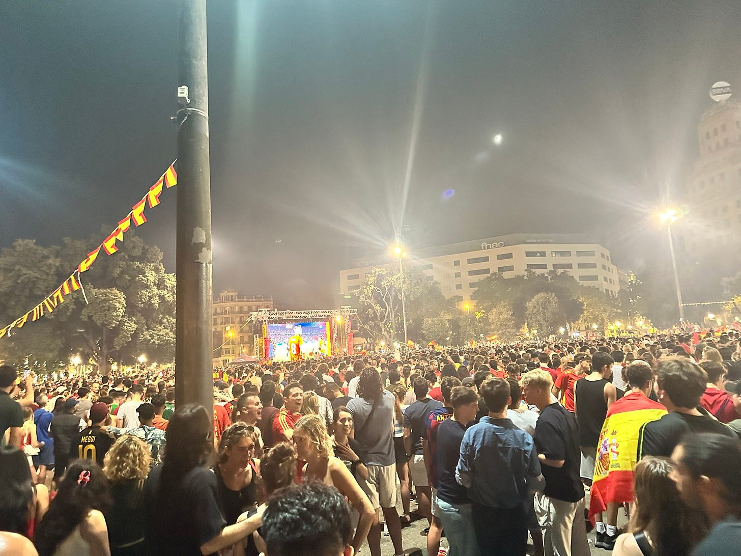 Thousands of fans in Spanish jerseys are watching a big screen broadcasting a football match