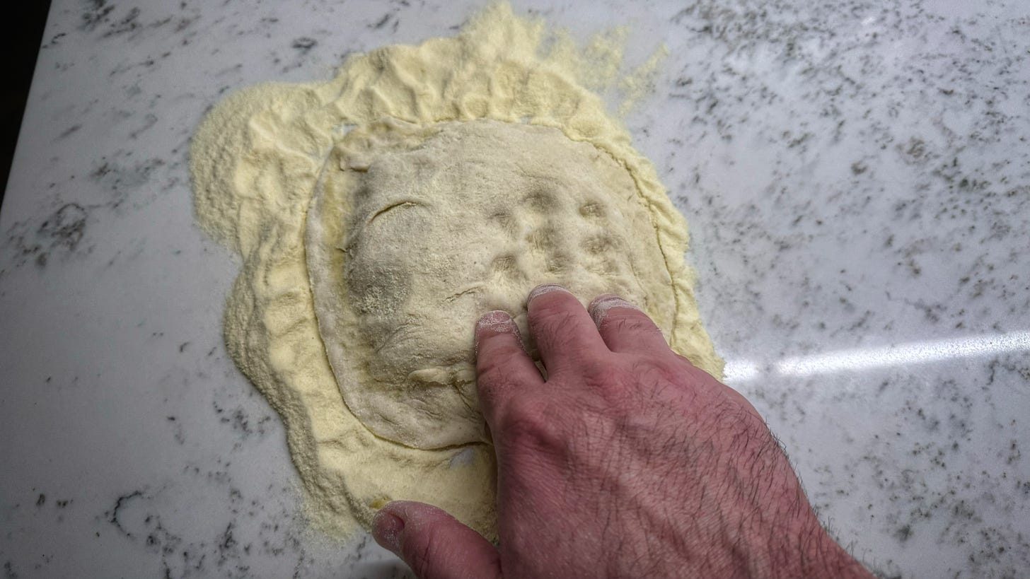 A hand dimpling the surface of a dough that is on top of a thick layer of semolina.
