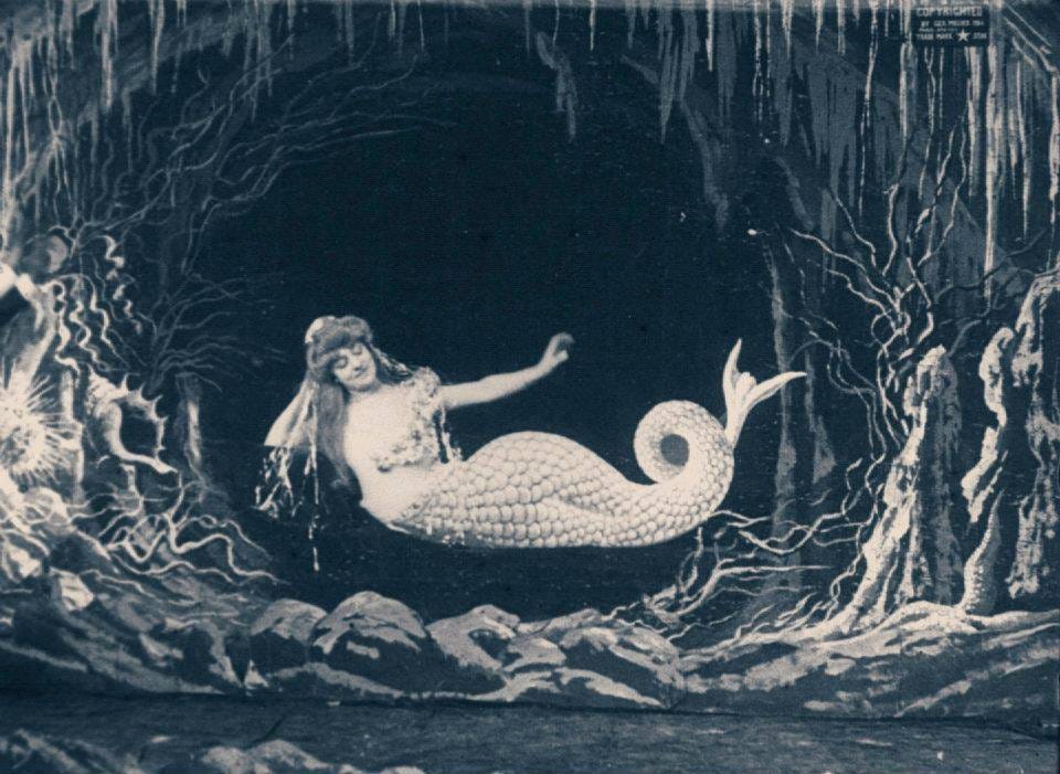 A still from an old black and white film featuring a mermaid in an underseas grotto, floating serenely on an underseas current and looking very pleased with herself.