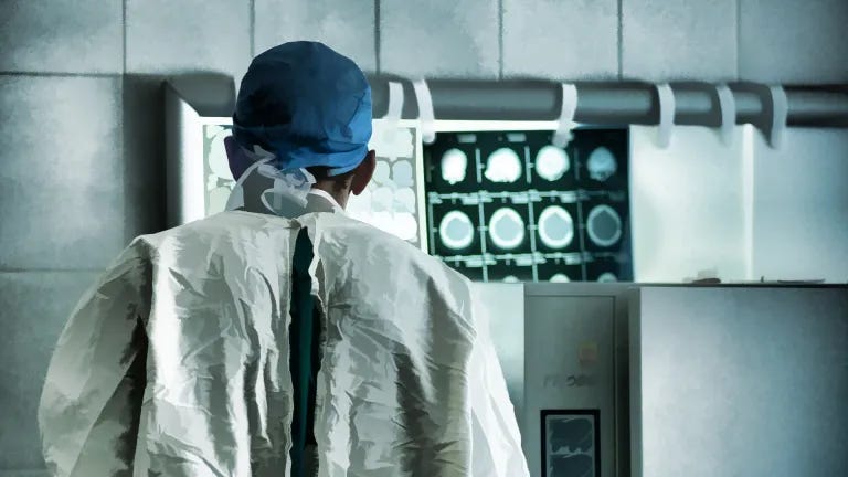 Ein Arzt steht in Schutzkleidung vor einem Gerät auf dem Röntgenaufnahmen zu sehen sind.