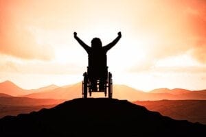 Person raising arms in triumph, in wheelchair, at top of hill