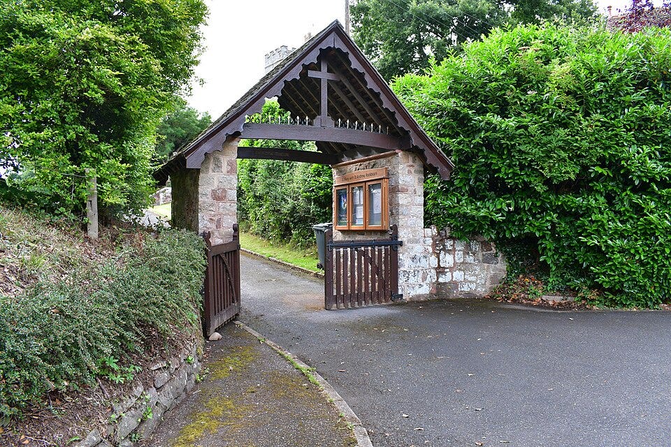 A brick built lychgate with a wooden roof. The wooden gate stands open. A brick built lychgate with a wooden roof. The wooden gate stands open.