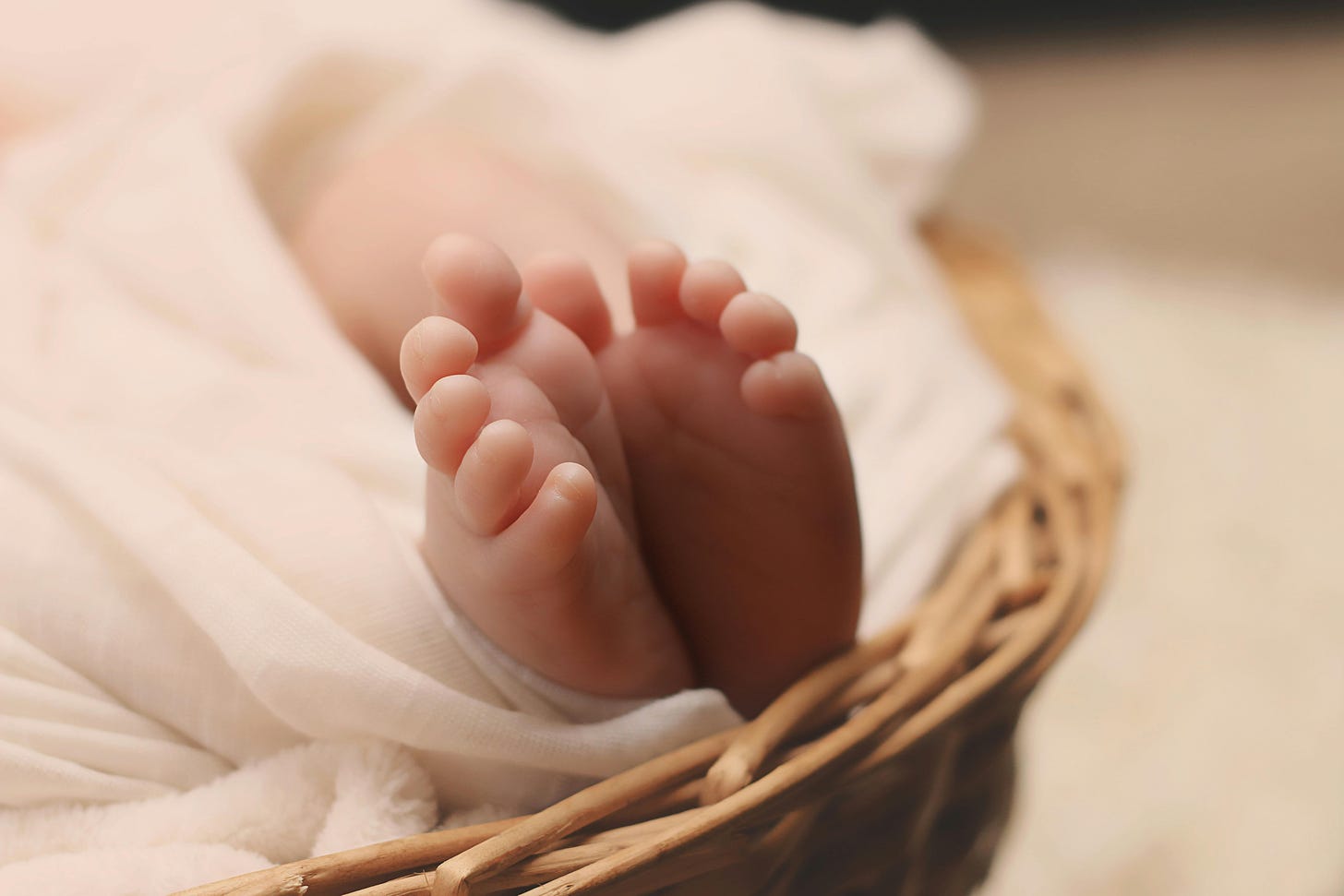 Free Adorable tiny newborn baby feet wrapped in a soft blanket inside a wicker basket. Stock Photo