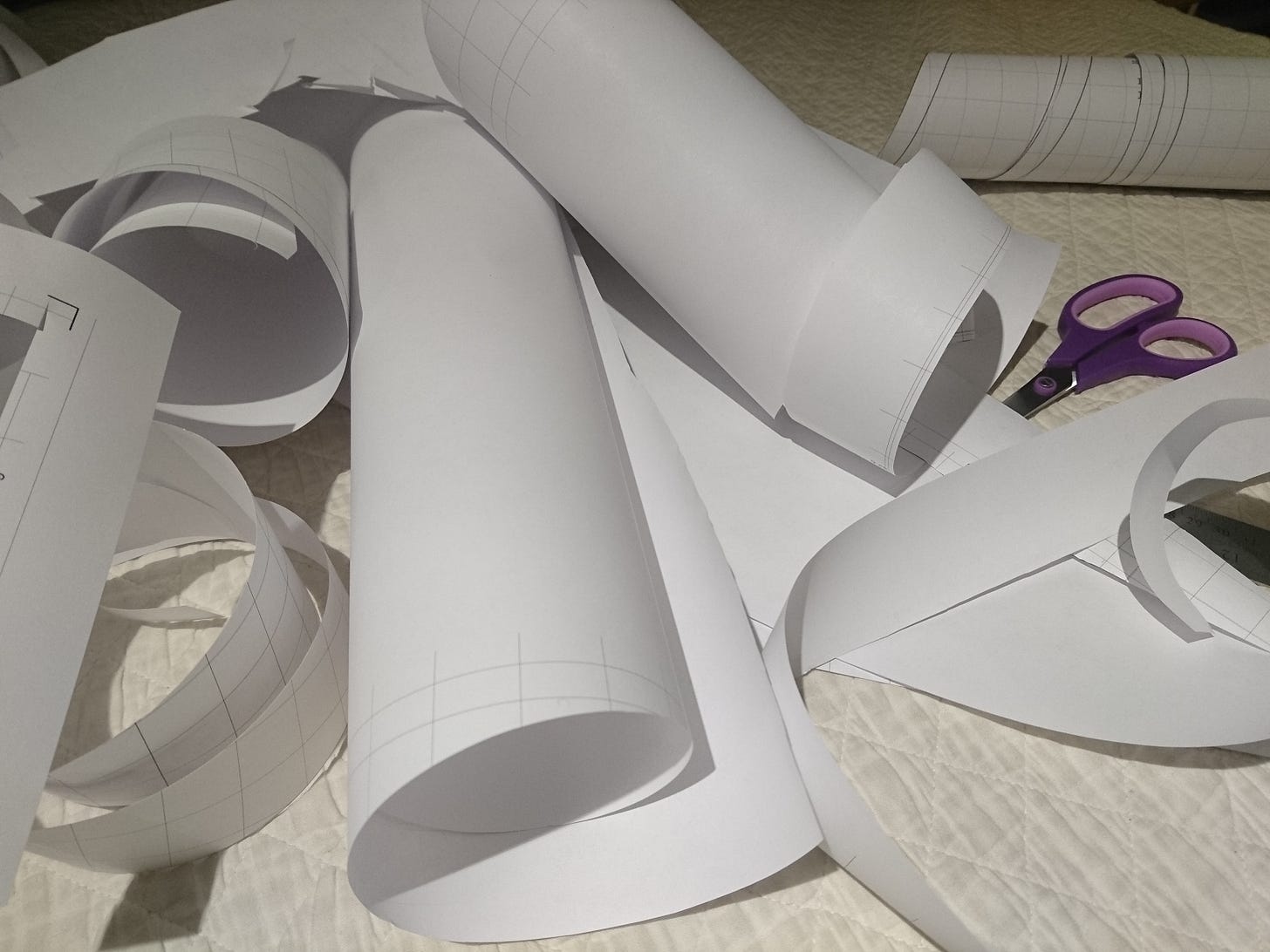 rolls of cut up pattern paper on white fabric. A pair of purple paper cutting scissors sits to one side