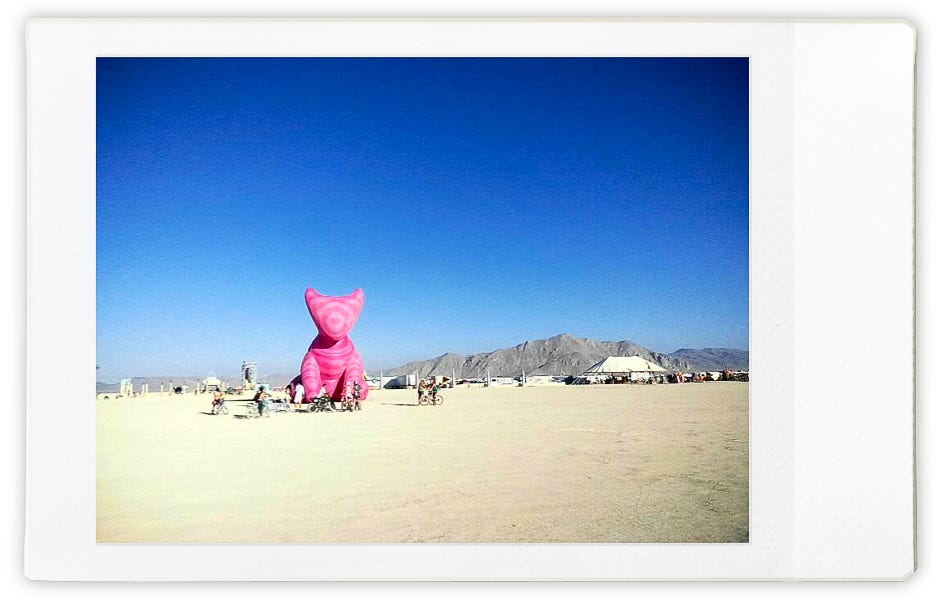 An enormous pink sculpture of a dog (I think?) dwarfing the mountains behind it 