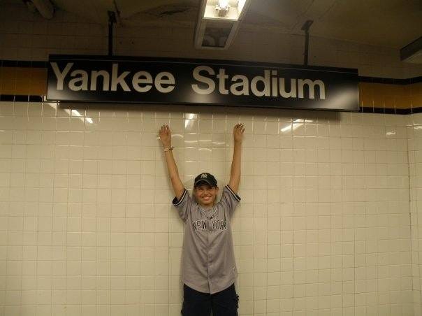 Jordan as a child, arms in the air and smiling underneath a subway sign that marks the stop for Yankee Stadium