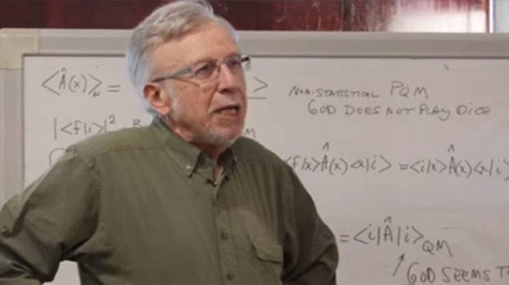 Man with glasses, white hair and green shirt in front of a white board full of equations