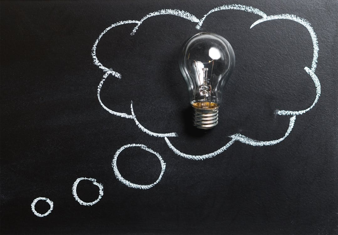 Free Light bulb laying on chalkboard with drawn thought bubble, symbolizing creative ideas. Stock Photo