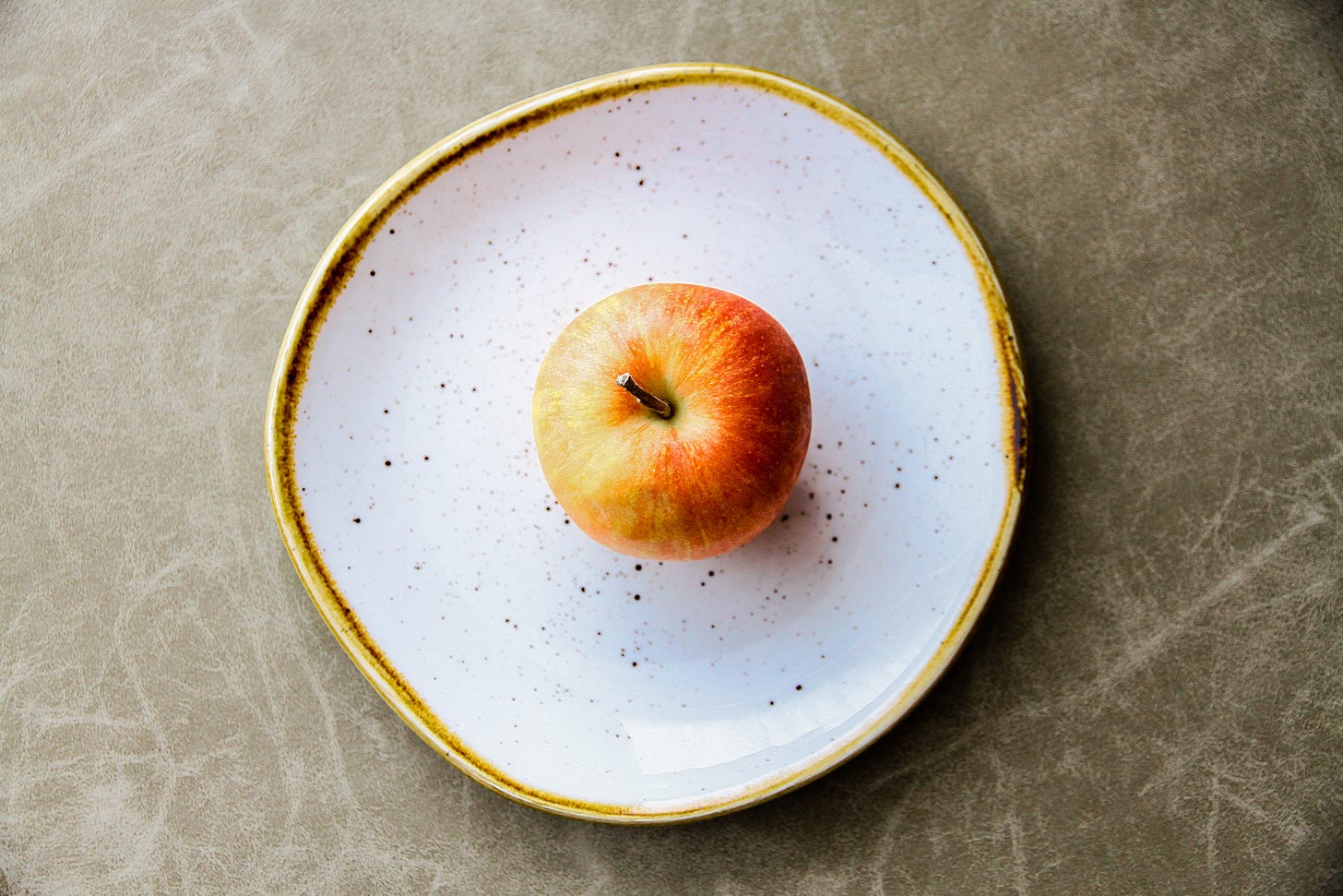 View from above of a red apple on a white plate with a gold rim.