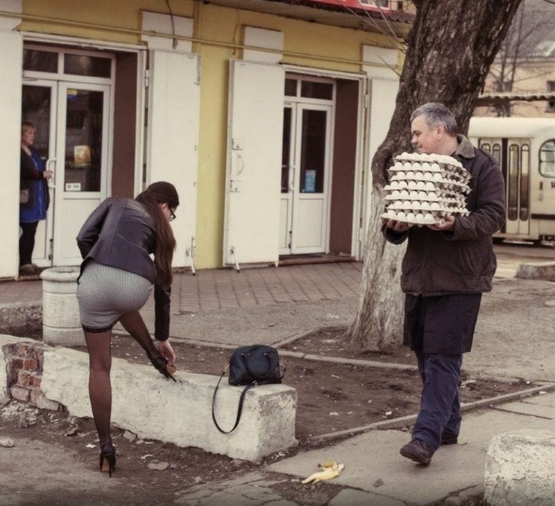 eastern europe: older middle-aged man carrying a bunch of eggs in loose cartons on the street, approaching a banana peel but distracted by a woman nearby