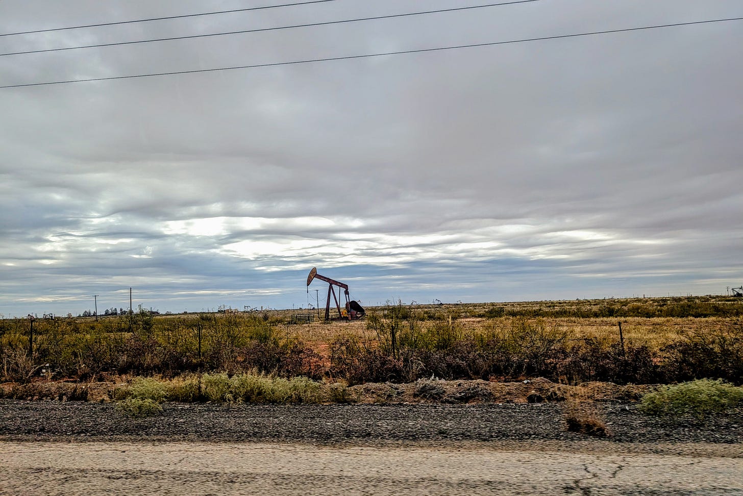 A small oil derrick stands in an open Texas field under an overcast sky A small oil derrick stands in an open Texas field under an overcast sky