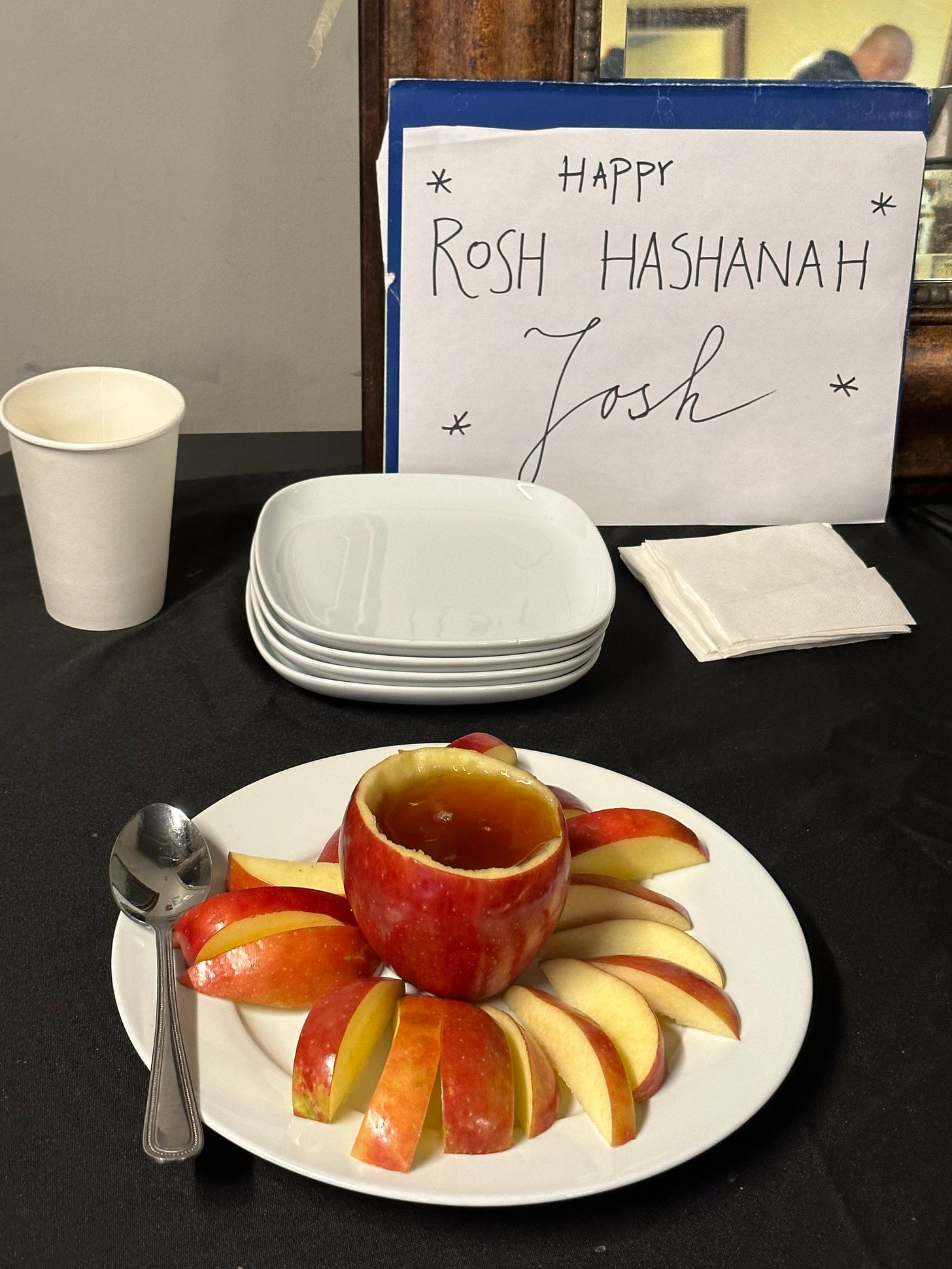 A "Happy Rosh Hashanah, Josh!" sign with some apples and honey. The honey is inside a hollowed-out apple.
