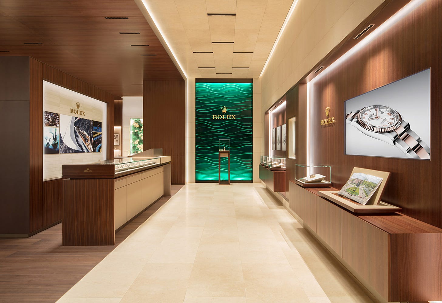 L'interno di una boutique Rolex. Il mood è estremamente minimalista: luci soffuse, col led a parete, mobili squadrati, bassi, in legno color ciliegio, un fondale verde col logo Rolex al centro, dorato. Qualche espositore in vetro, pochissimi poster alle pareti.