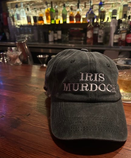 On a bar there's a green baseball cap with white lettering that says Iris Murdoch.