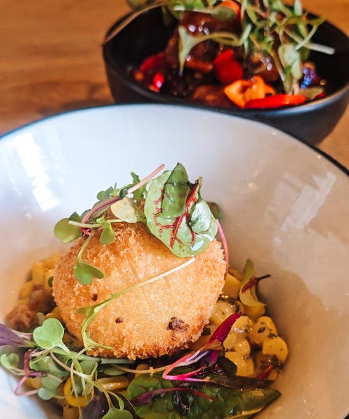 Two plates - one with an arancini ball and salad and one with fried chicken
