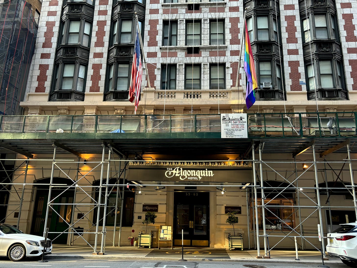 The exterior of the Algonquin from across 44th Street. There is green scaffolding over the awning and the American and Pride flags hanging outside.