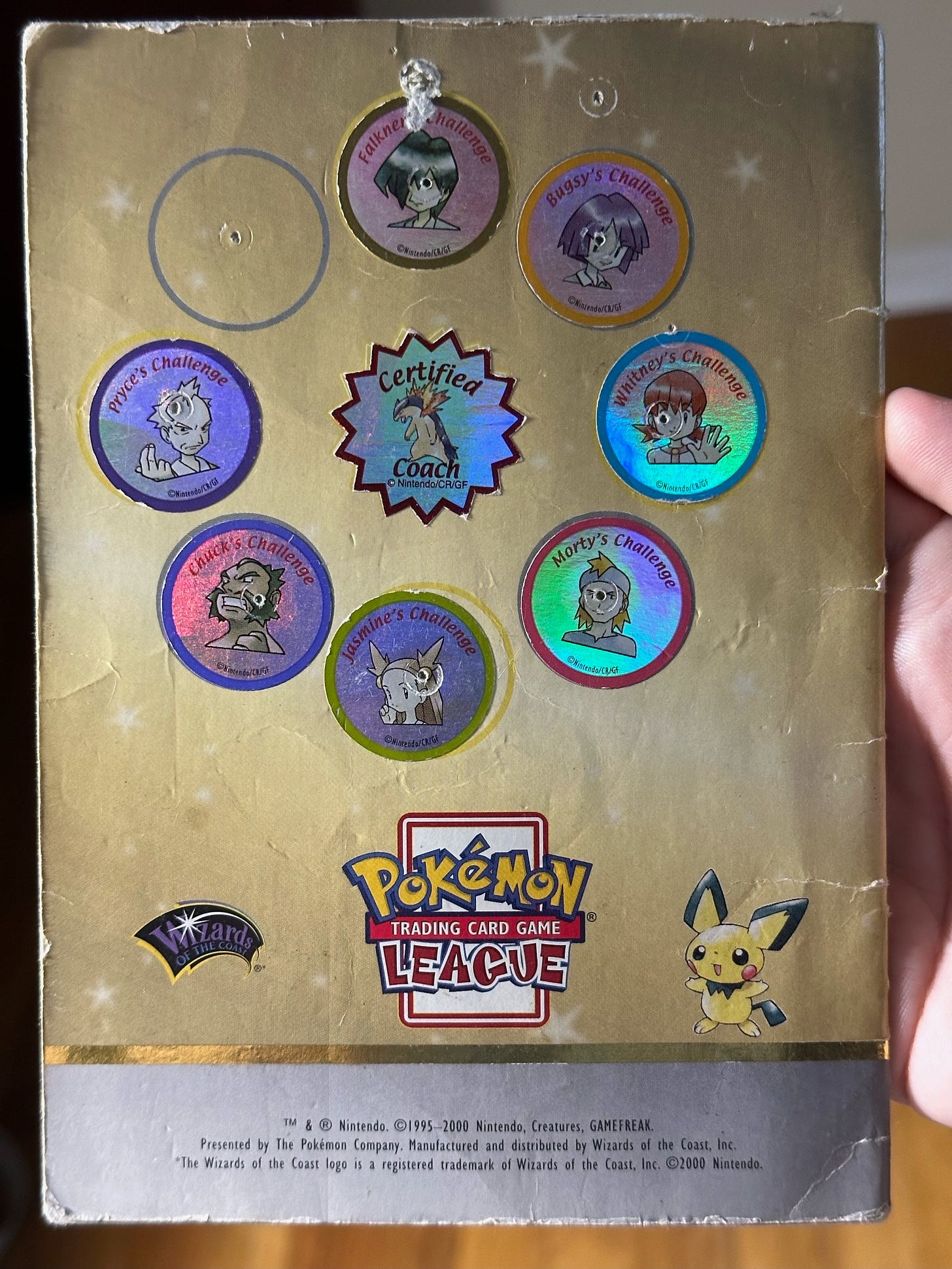 The back of Greg's Badge Book, which contains seven out of eight gym badges, and a special "Certified Coach" badge