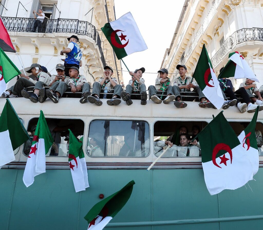 Boys sit on a bus waving Algerian flags.