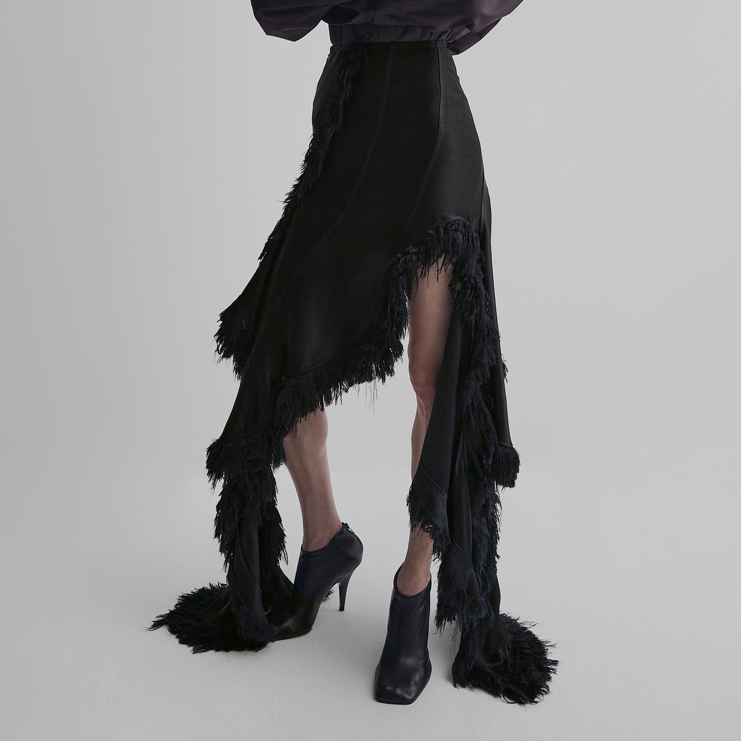 Front view of model wearing hand-combed embroidered sliced skirt in black viscose with black heeled boots.