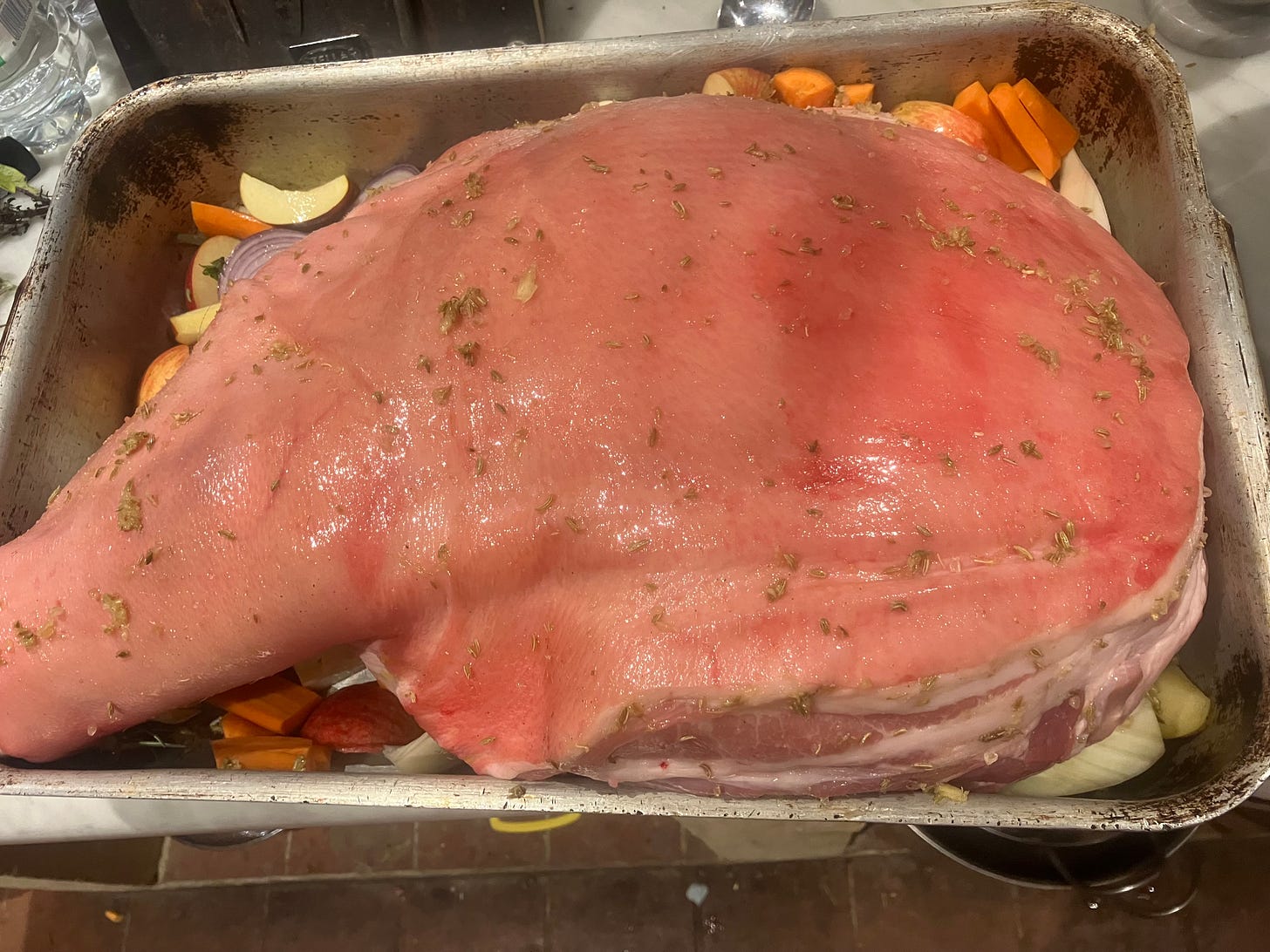Whole shoulder of pork on a bed of vegetables ready to go into the oven