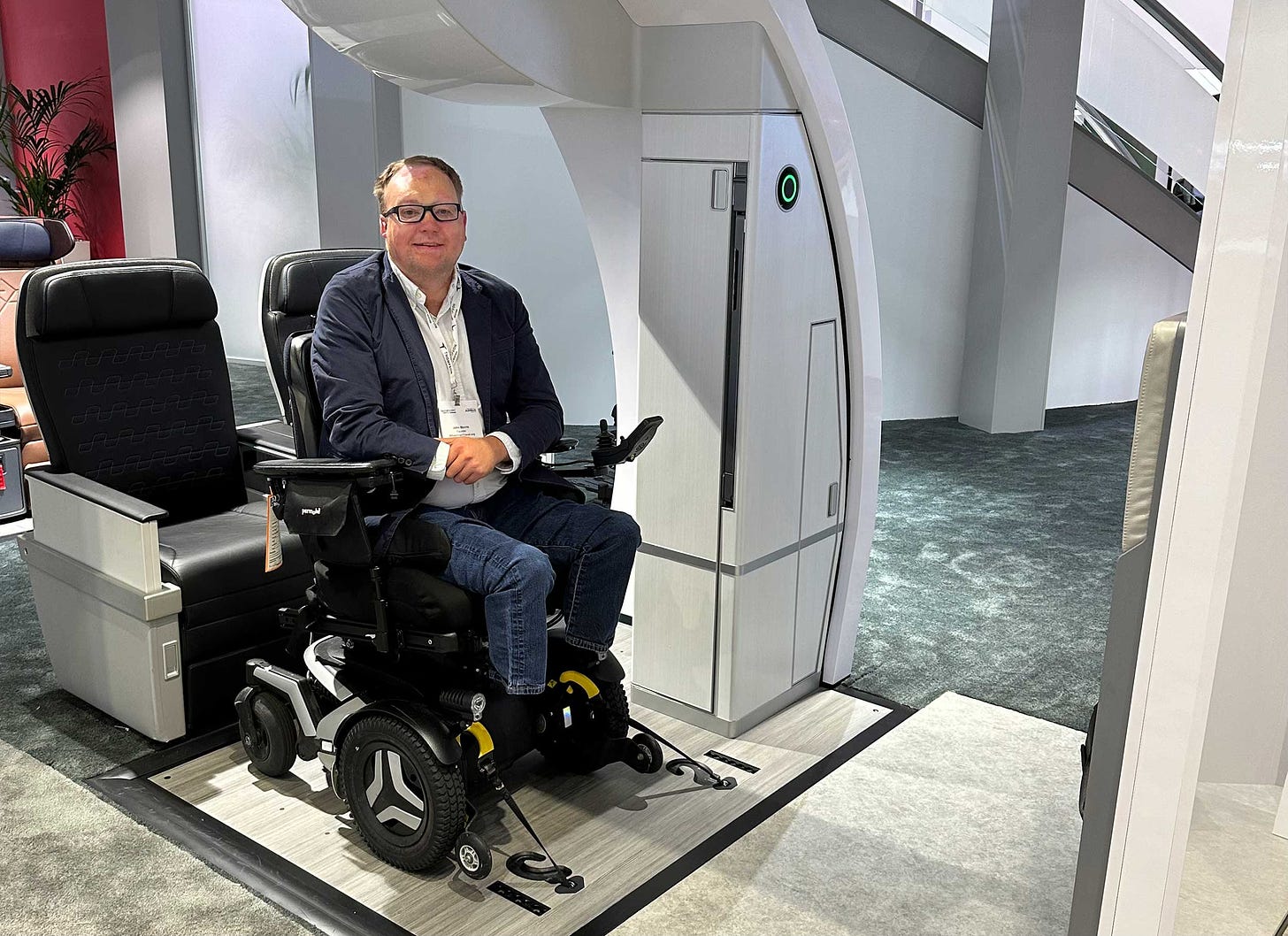 John seated in his wheelchair onboard an airplane mock-up with his chair secured to the floor using straps.