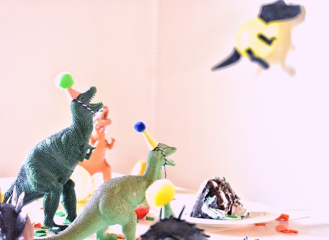 Toy dinosaurs in party hats and cake on table