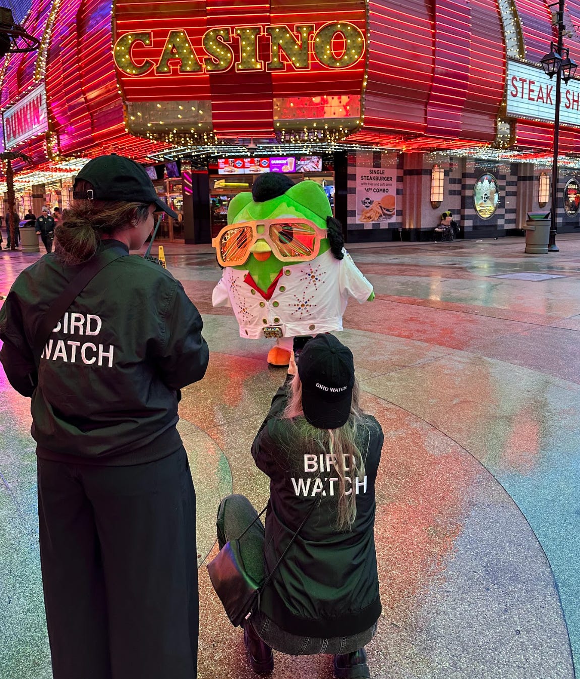 Duolingo owl dressed as elvis in Las Vegas with team members capturing content wearing shirts that say "BIRD WATCH"