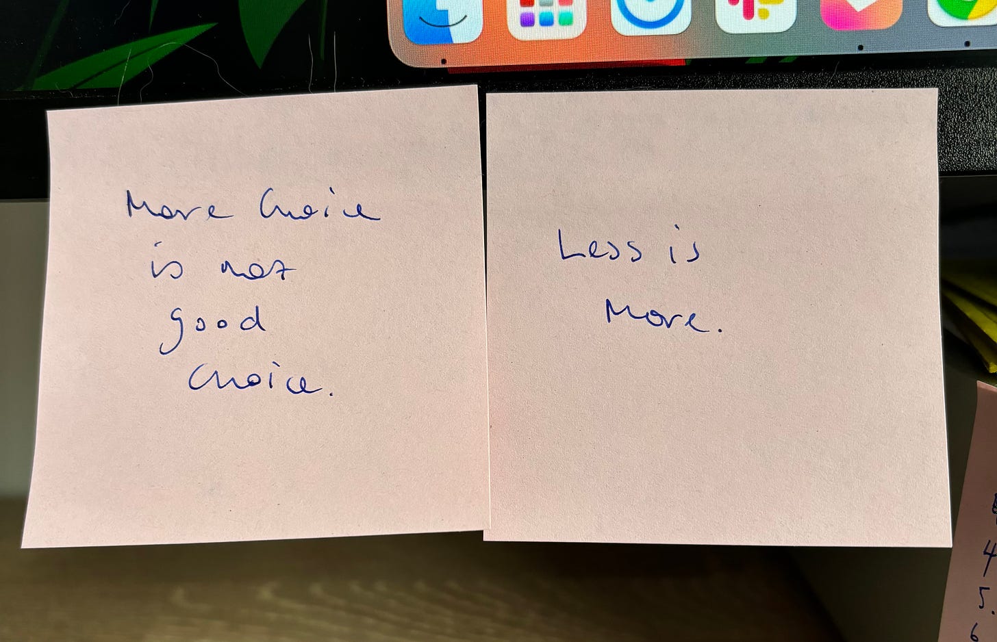 Two pink post-it notes stuck to a monitor. The first says More choice is not good choice and the second says Less is more.