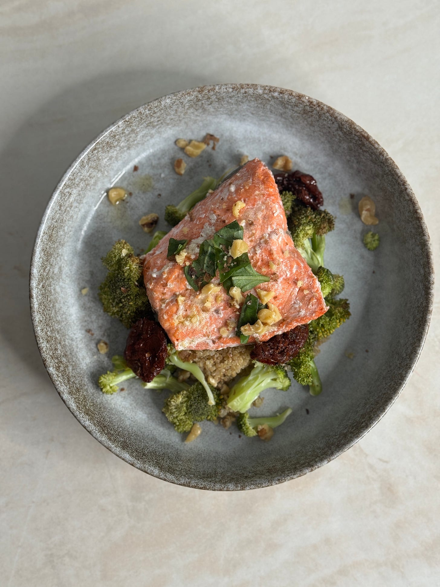Sockeye salmon fillets pan-seared with spices, served alongside roasted broccoli, quinoa, sun-dried tomatoes, toasted walnuts, and fresh basil.