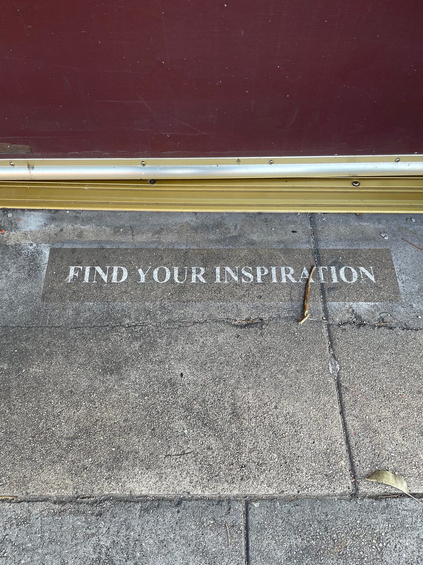 A section of pavement next to the bottom of a maroon doorway where the words "Find your inspiration" have been stenciled in.